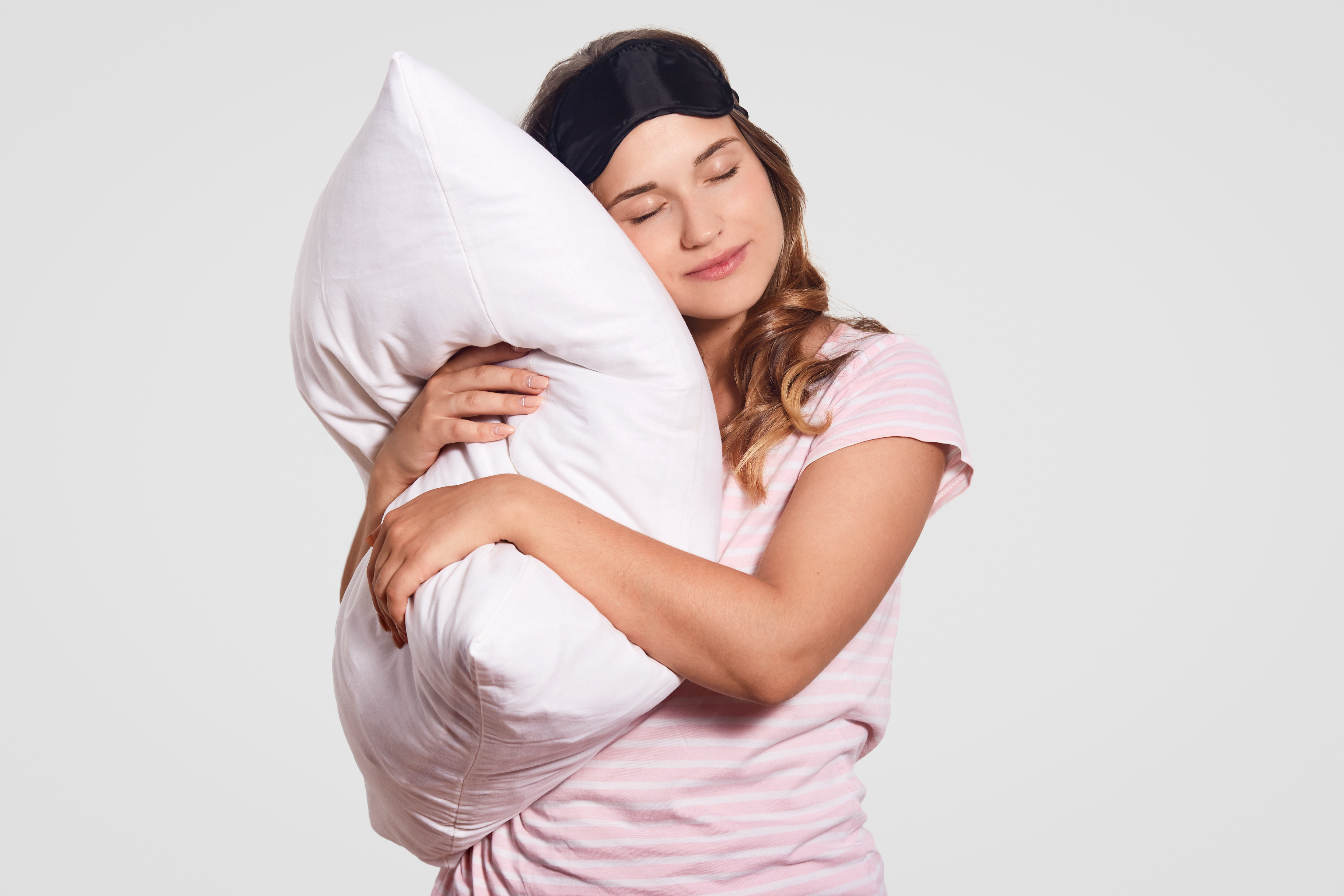 photo-of-european-woman-with-healthy-skin-leans-on-soft-pillow-wears-pyjamas-eyewear-on-head-poses-alone-on-white-has-sleepy-look-people-good-morning-concept